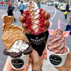 three ice cream sundaes with toppings in their hands on the street corner