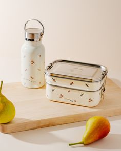 two pears on a cutting board next to a lunch box and a glass bottle