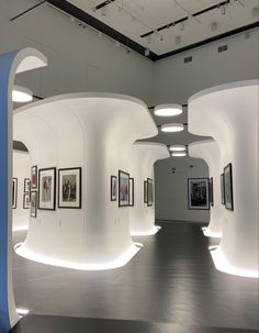 an art gallery with white curved walls and pictures on the wall, all lit up