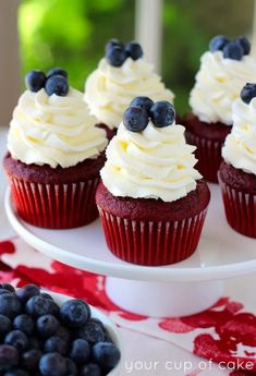 red velvet cupcakes with white frosting and blueberries on a cake plate