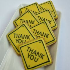 four yellow thank you cookies with black writing on them are sitting in a white tray