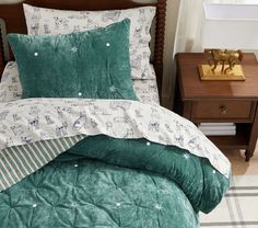 a bed with green comforter and pillows on top of it next to a night stand