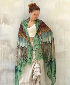 a woman standing in front of a white wall wearing a green jacket with large wings