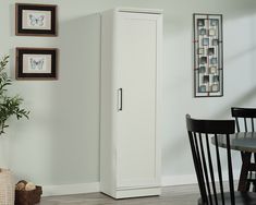 a tall white cabinet next to a dining room table and chair with pictures on the wall