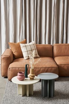 a couch and two tables in front of a curtained window with curtains behind it