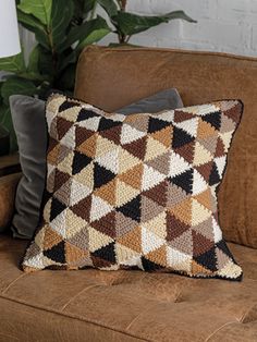 a brown couch with two pillows on it and a plant in the corner next to it