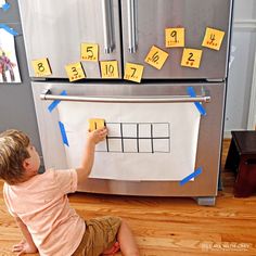 a young boy sitting on the floor in front of a refrigerator with magnets attached to it