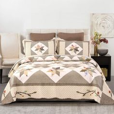 a bed covered in a quilt and pillows next to a white chair with flowers on it