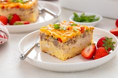 two white plates with food on them and strawberries in the foreground, one has a piece of casserole