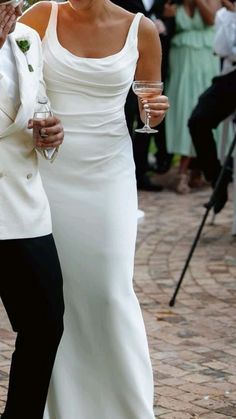 a man and woman walking down the street holding wine glasses in their hands while wearing formal attire