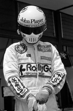 a man in a racing suit and helmet is holding his hand out to the side