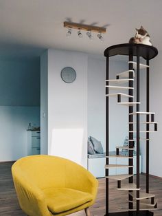 a cat sitting on top of a tower next to a yellow chair in a living room