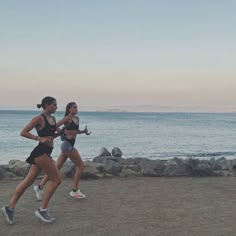 two women running on the beach at sunset or sunrise with water and rocks in the background