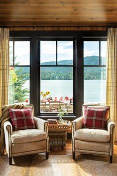 two chairs and a table in front of a large window with lake view on the other side