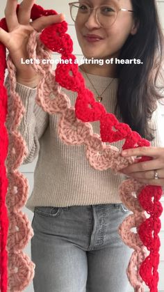 a woman wearing glasses holding up a red crochet scarf with the words, love is not a string of hearts