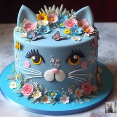 a blue cake decorated with flowers, butterflies and a cat's face