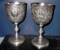 two silver goblets sitting on top of a black table next to a blue wall