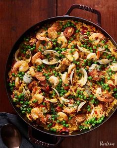 a skillet filled with shrimp, rice and peas on top of a wooden table