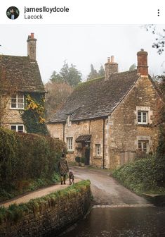 a man walking his dog on a path in front of some old stone houses and water