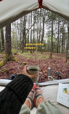 someone is sitting in a tent with their feet up on the bed and holding a cup