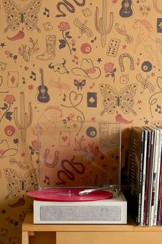 a record player sitting on top of a wooden table next to a wallpapered wall