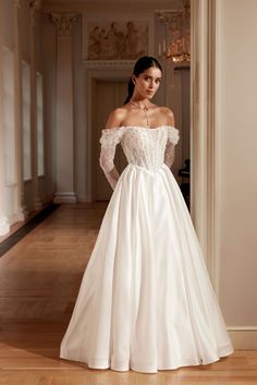 a woman in a white wedding dress standing on a wooden floor with an open doorway