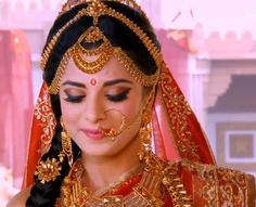 a woman in a red and gold bridal outfit with her eyes closed, looking down at the camera