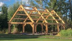 a large wooden structure sitting in the middle of a lush green field next to trees