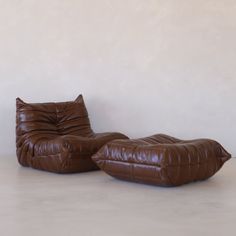 a brown leather chair and footstool sitting next to each other in front of a white wall