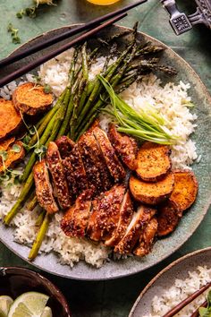 a plate filled with meat, rice and asparagus next to chopsticks