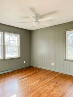 an empty room with wood floors and two windows in the wall, painted gray green