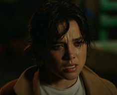 a close up of a person wearing a trench coat and looking at the camera with tears on her face