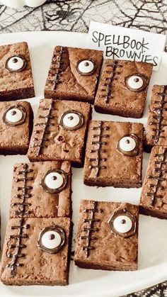 some brownies with googly eyes are on a white plate and there is a sign that says spell book browns