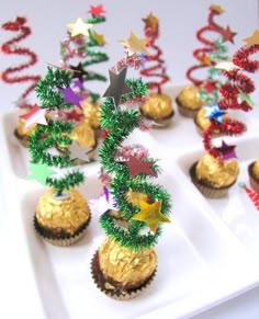 cupcakes decorated like christmas trees on a white tray with red and green decorations