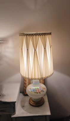 a lamp sitting on top of a table next to a white vase with flowers in it