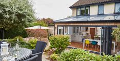 an outdoor dining area with table and chairs in front of a house that is surrounded by greenery