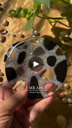 a person holding up a glass ornament with black and silver circles on it