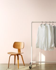 a white shirt hanging on a rail next to a chair and a rack with clothes