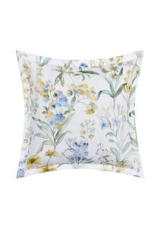 a white pillow with blue, yellow and green flowers on the front is sitting on a white background