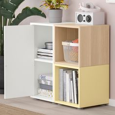 a book shelf with books, magazines and a radio on it next to a potted plant