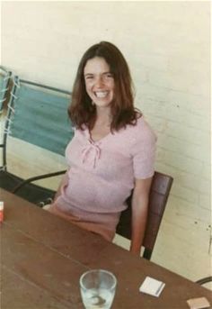 a woman sitting at a table with a glass of water in front of her smiling