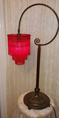 a lamp with a red shade on top of it next to a white table cloth