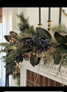 a fireplace mantel decorated with greenery and pine cones, evergreens, berries and lights