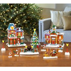 christmas decorations and figurines on a wooden table in front of a decorated christmas tree