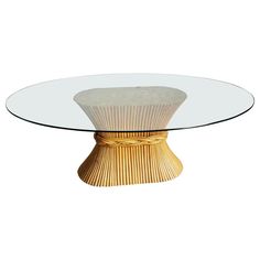 a round glass table with an intricate design on the top and base, in gold