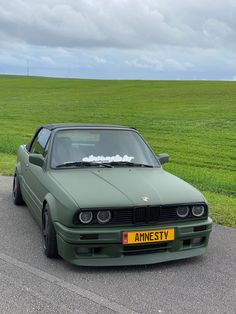 a green car parked on the side of a road next to a lush green field