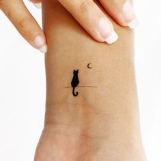 a woman's wrist with a small black cat tattoo on the left side of her arm