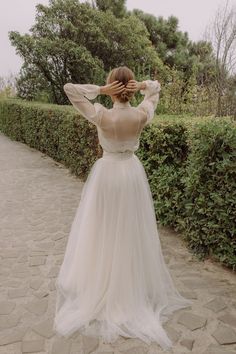 a woman in a long white dress is standing on a cobblestone path with her back to the camera