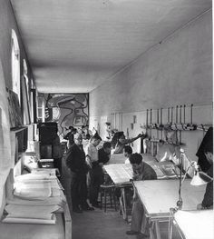 black and white photograph of people working at desks in a room with lots of papers