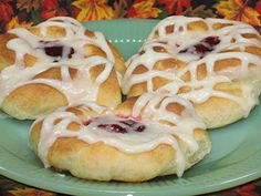 three cranberry rolls on a green plate with white icing and some leaves